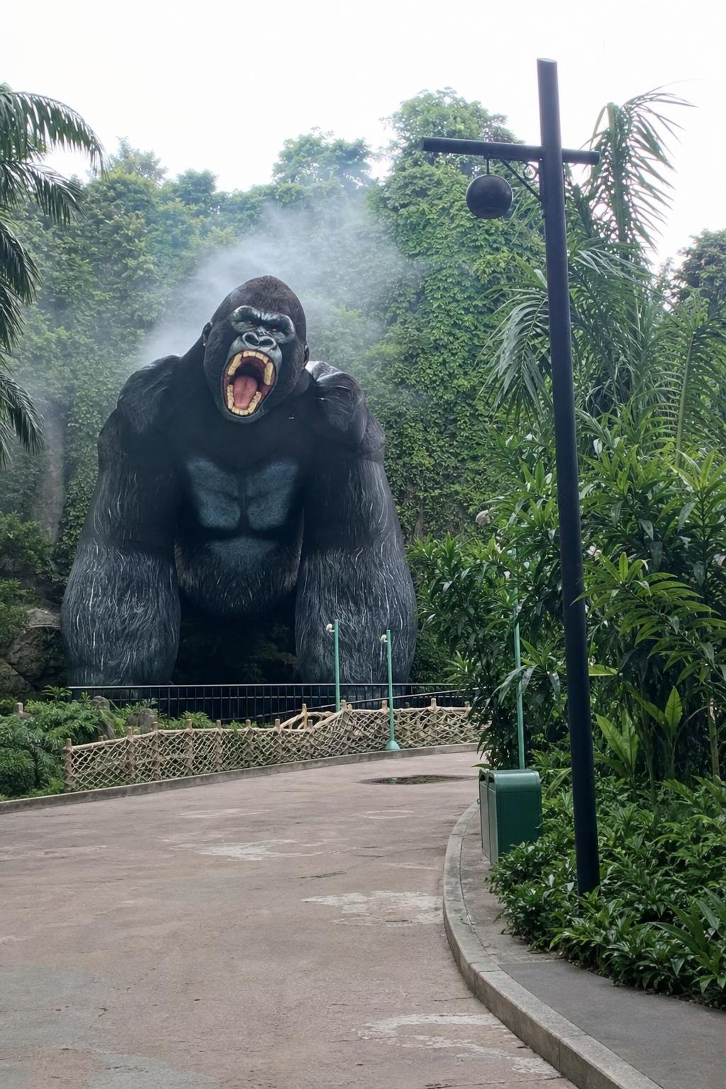 The gorilla inflatable seen from far down the empty jungle path, towering over the rope net in the mist