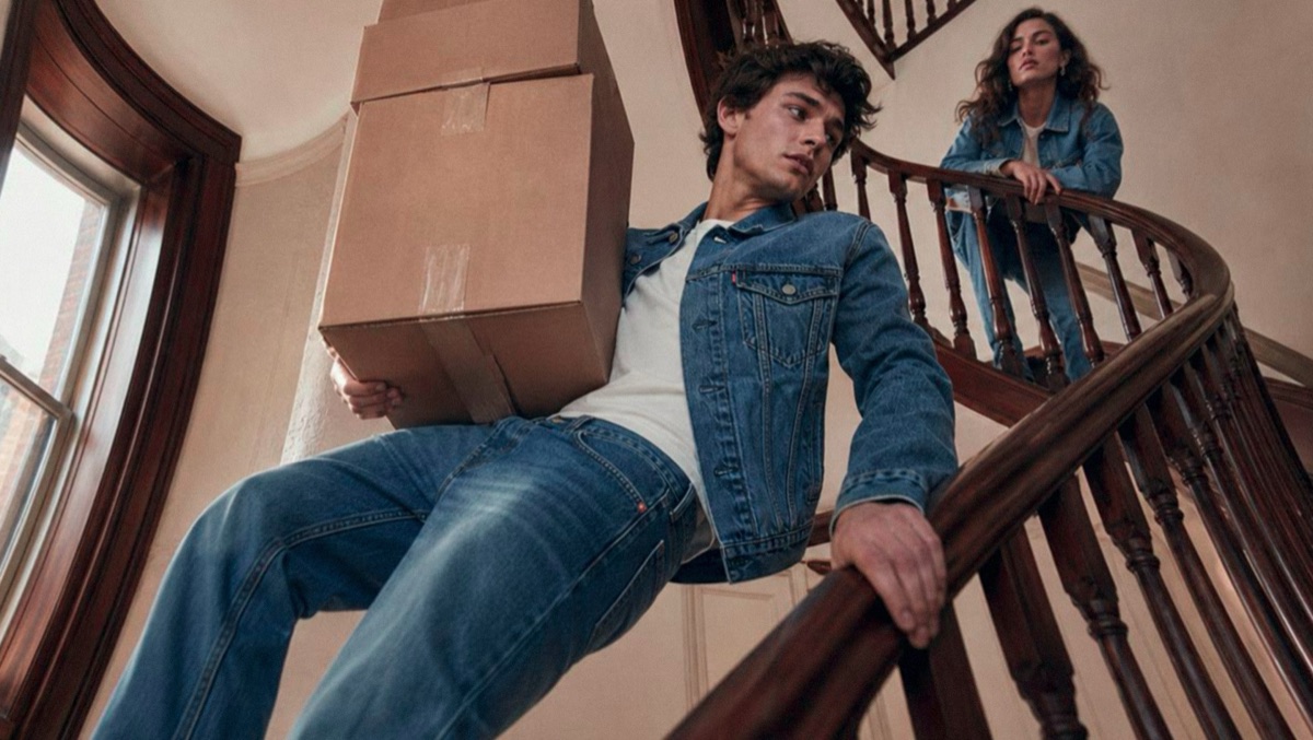 A model sliding down a brownstone banister holding moving boxes