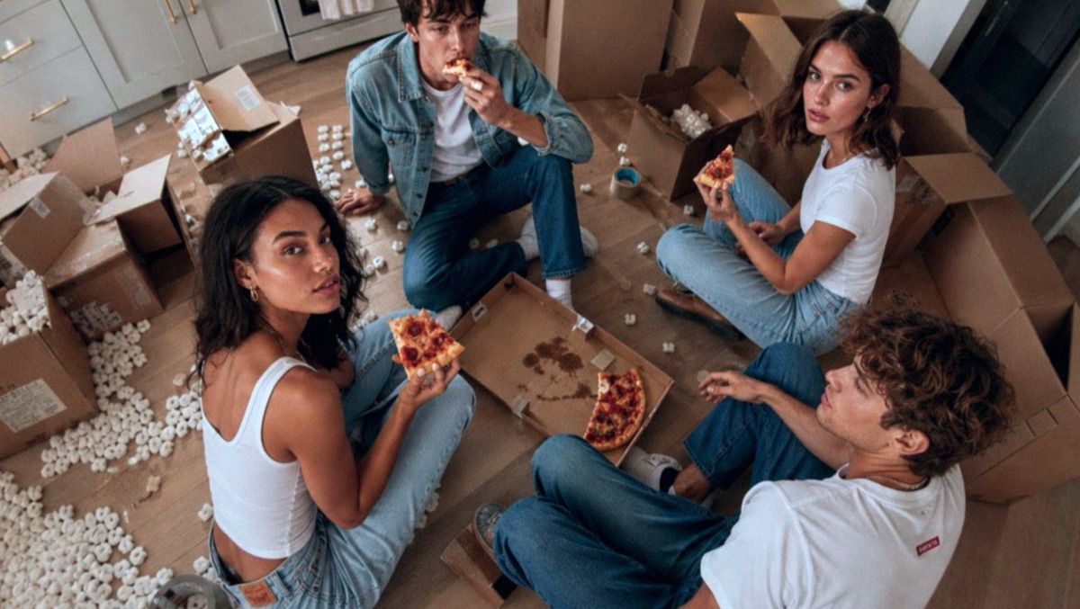 Friends in Levi's eating pizza on the floor between open moving boxes