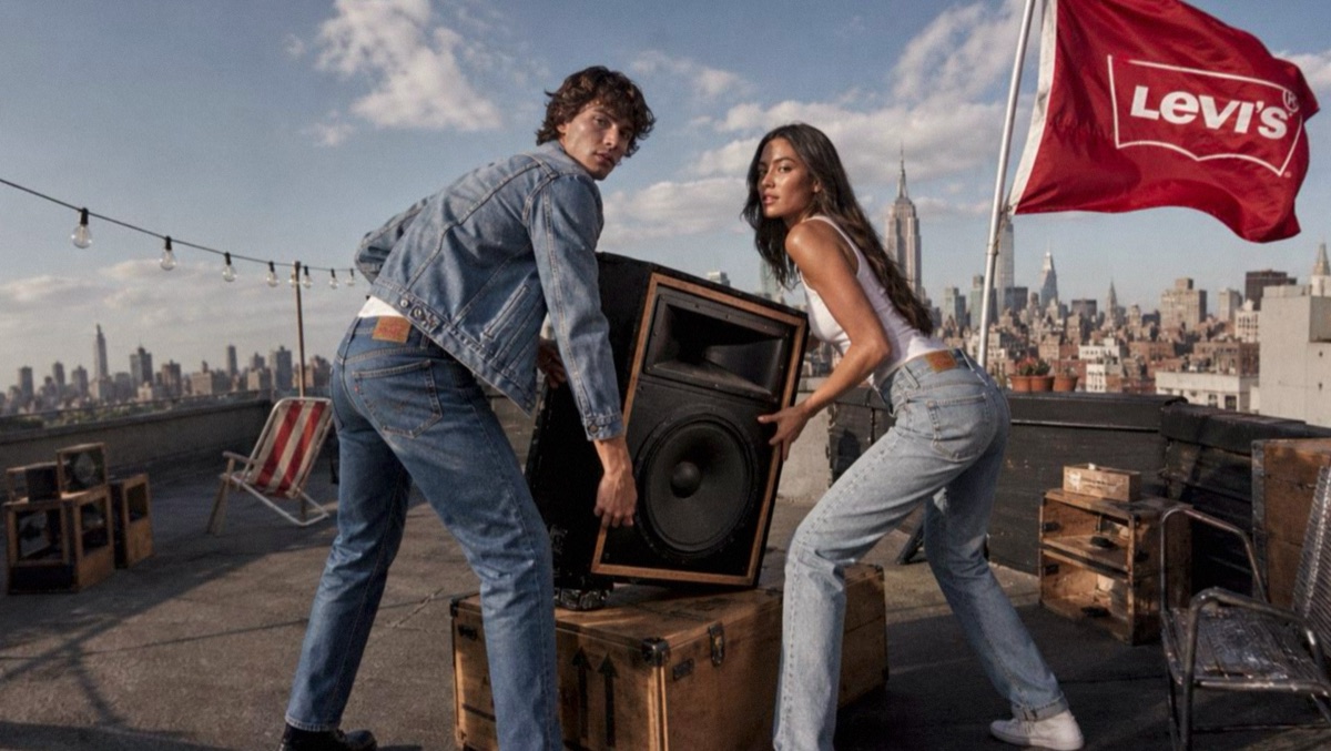 Two models lifting a big speaker on a rooftop with a red Levi's flag and the city skyline